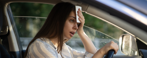 Frau in Auto wischt sich Schweiß ab